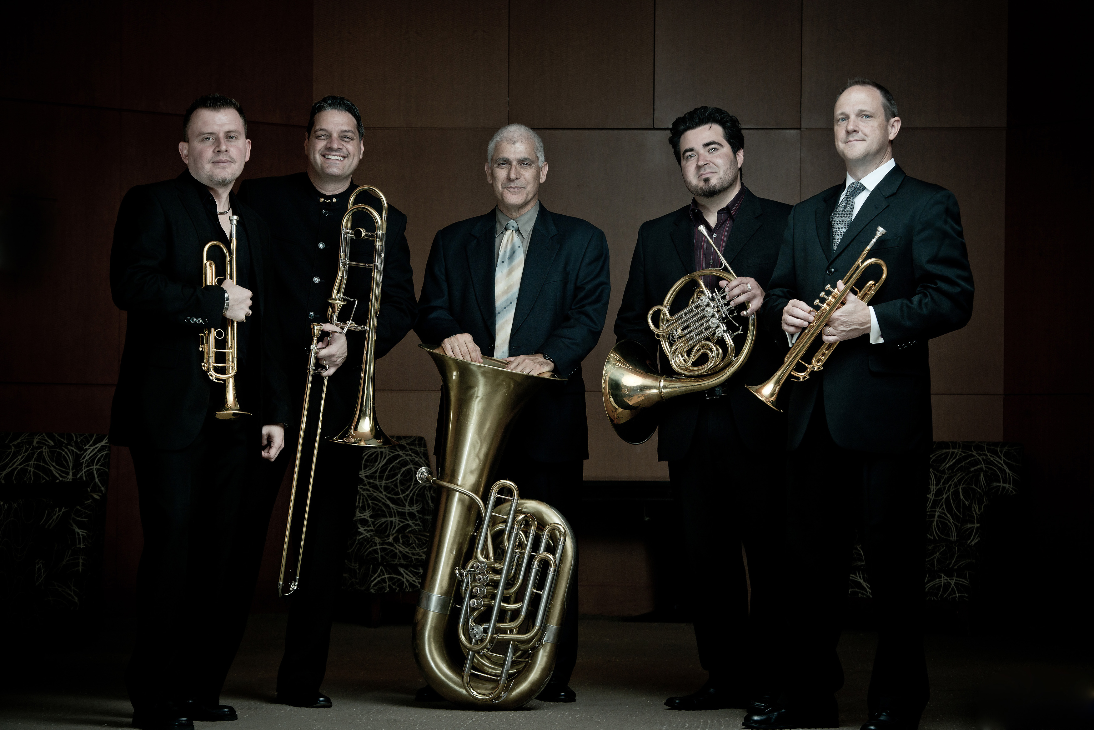 Photo of Boston Brass members in black tuxedos with brass instruments.