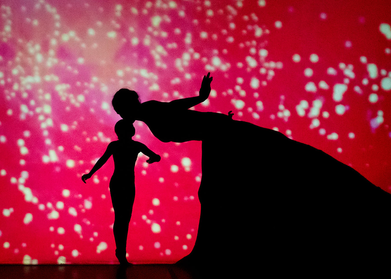 Silhouettes of woman kissing child on the head against red, sparkly background.